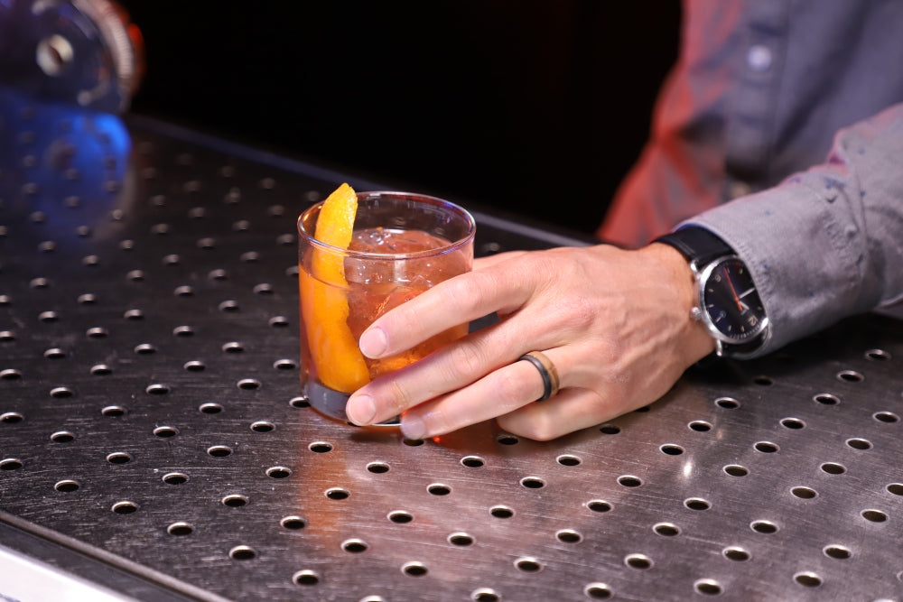 An old fashioned cocktail with the bartender wearing a whiskey barrel wood ring