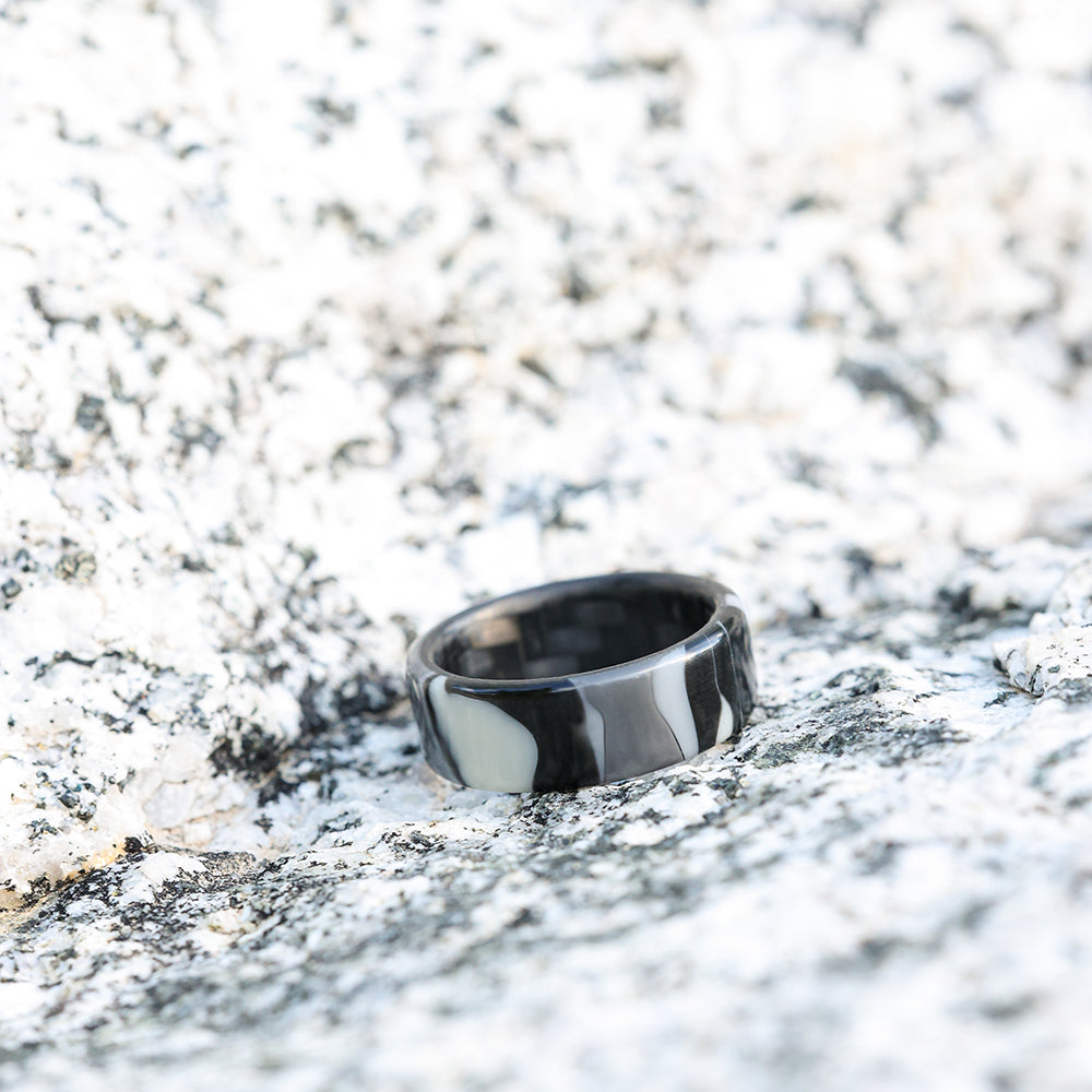 black camo wedding ring with carbon fiber sleeve on black and white speckled rocks