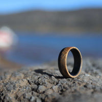 Men's whiskey barrel ring with carbon fiber outside on a rock