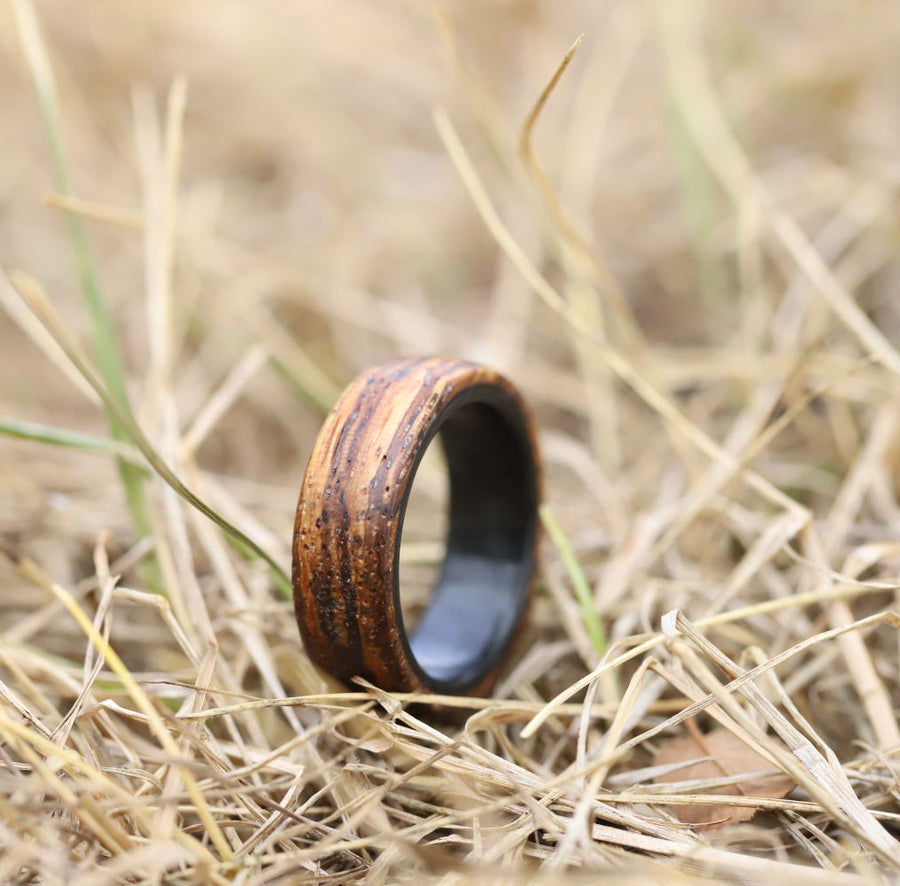 Zebra Wood Ring with Carbon Fiber Sleeve In A Field