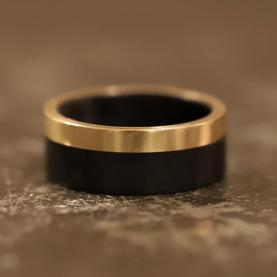 Men's carbon fiber ring with yellow gold band laying flat close up
