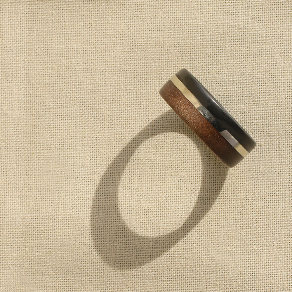 walnut wood and 14 karat gold wedding ring with carbon fiber sleeve on canvas