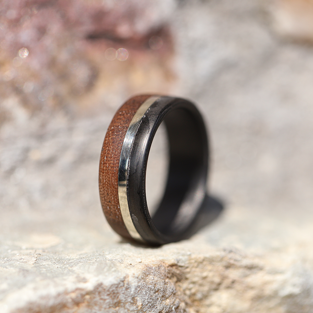 walnut wood and 14 karat gold wedding ring with carbon fiber sleeve on a rock