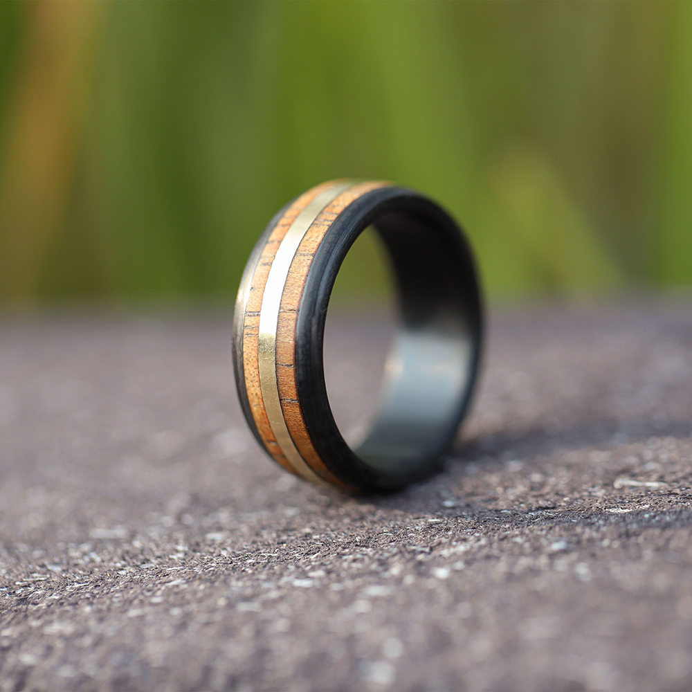 hawaiian koa wood ring with a gold inlay and carbon fiber sleeve on pavement